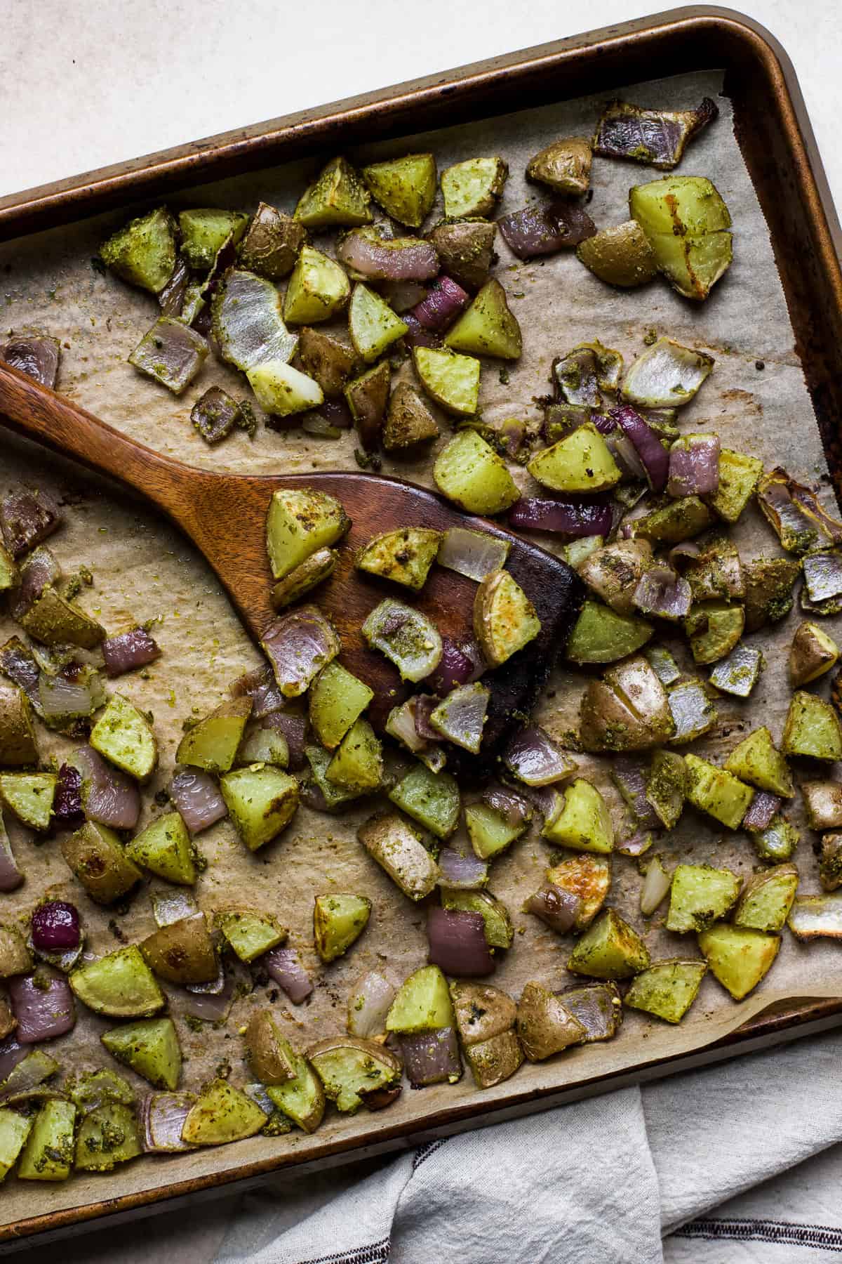 Pesto roasted potatoes on sheet pan with wooden turner.