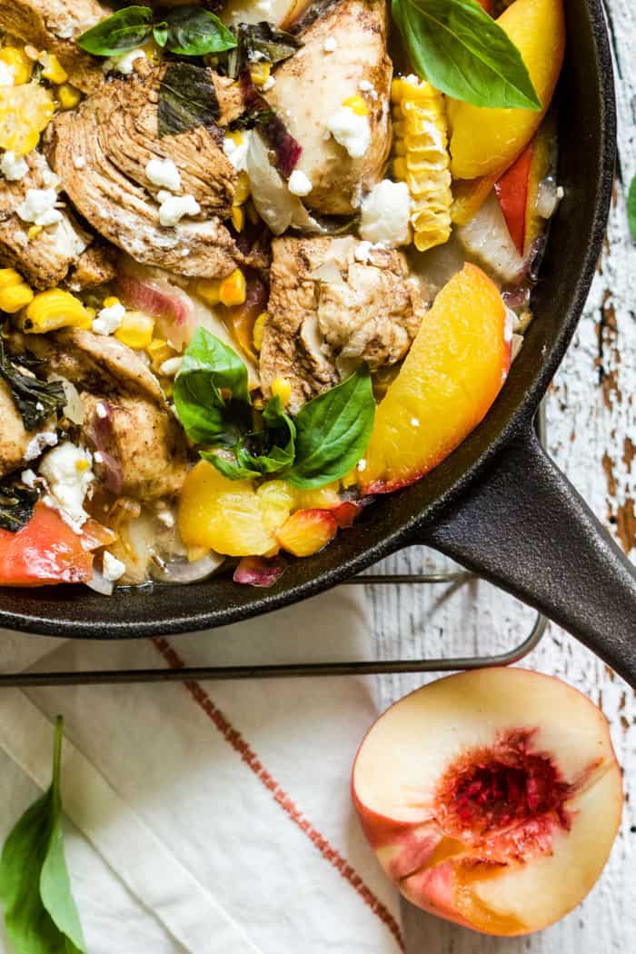 Peach basil balsamic chicken in a cast iron skillet with fresh basil and goat cheese, on top of a white linen napkin on a white farmhouse-style surface