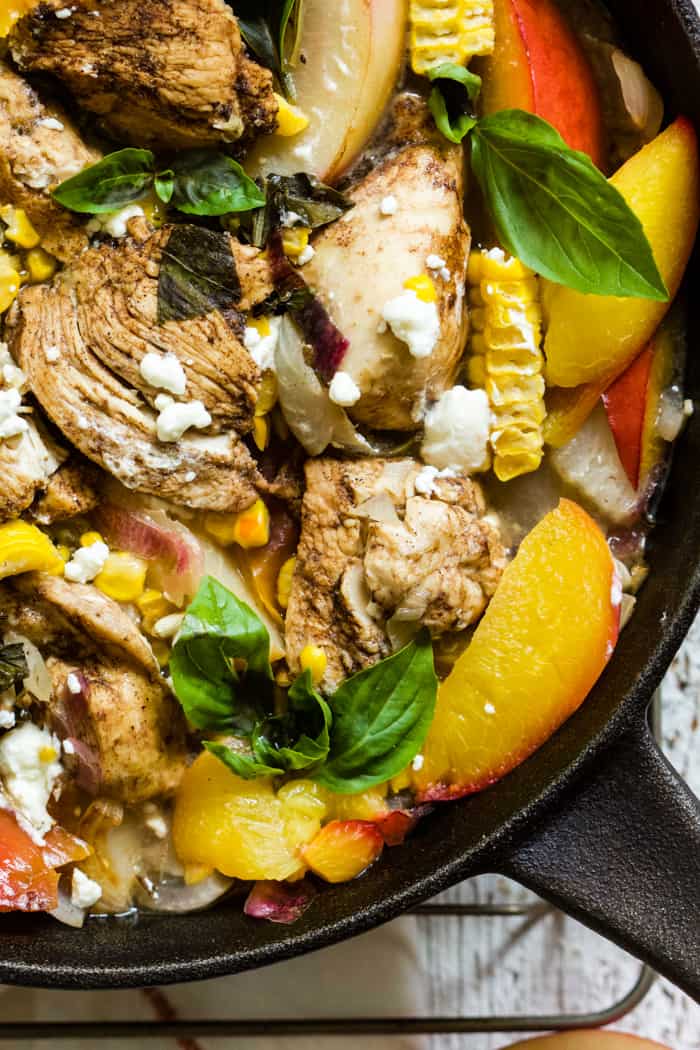 Peach basil balsamic chicken in a cast iron skillet with fresh basil and goat cheese, on top of a white linen napkin on a white farmhouse-style surface