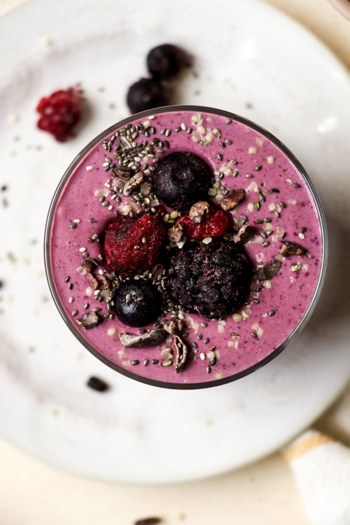 High protein berry smoothie in a glass, topped with berries, chia seeds, and cacao nibs.