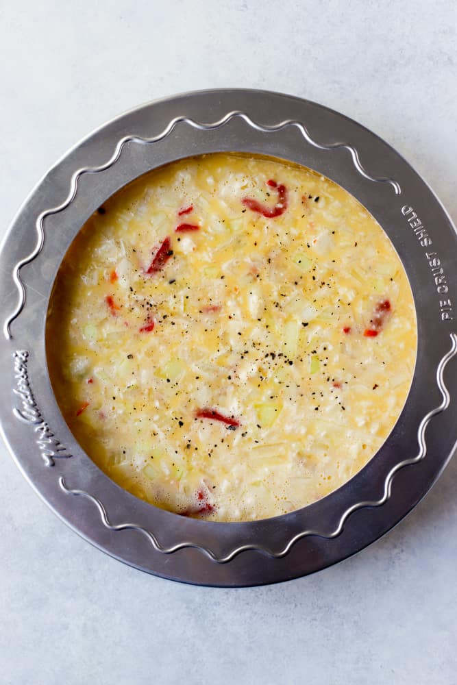 Quiche filling in pie dish with crust, with pie crust shield over the top