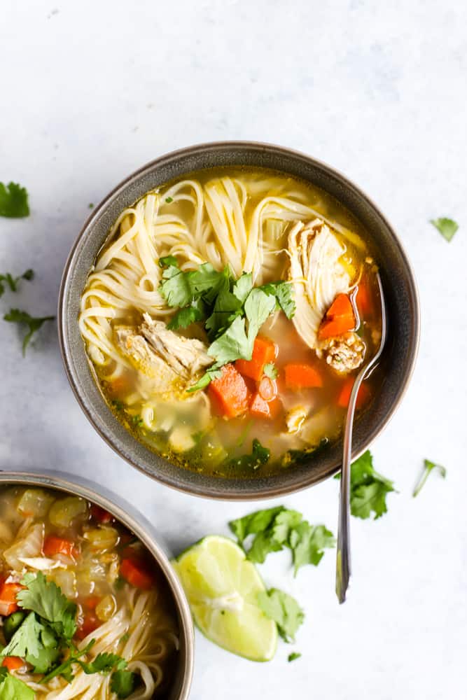 Ginger lime chicken noodle soup in a bowl topped with cilantro and squeezes of fresh lime juice,