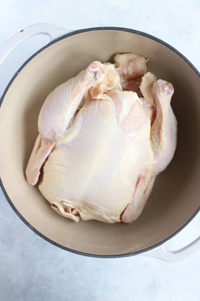 Whole uncooked chicken in a dutch oven, ready for making homemade chicken broth.