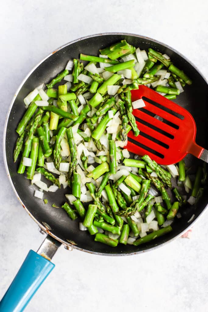 Sautéing asparagus and onion in a pan.
