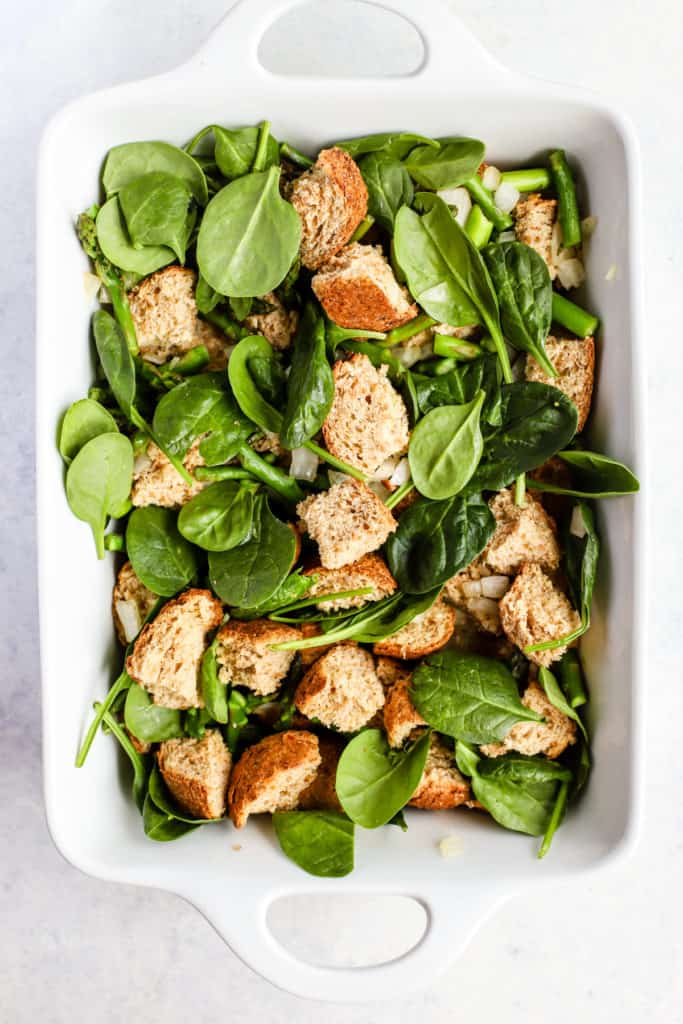 Bread cubes, veggies, and cheese in baking pan for spring breakfast strata.