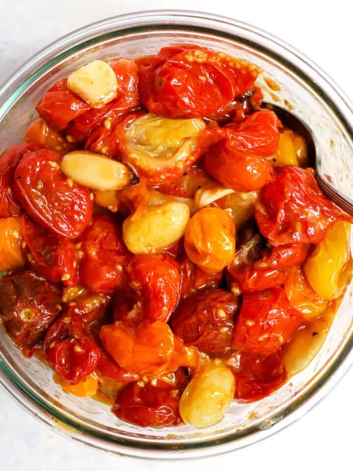 Garlic roasted tomatoes in glass bowl with spoon.