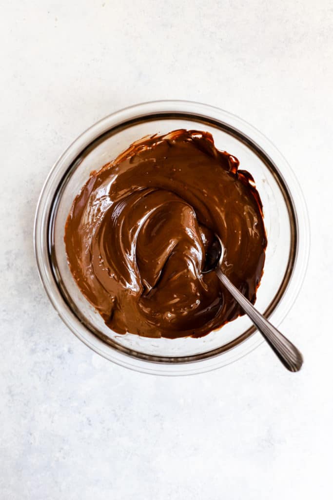 Melted dark chocolate in small clear glass bowl with spoon