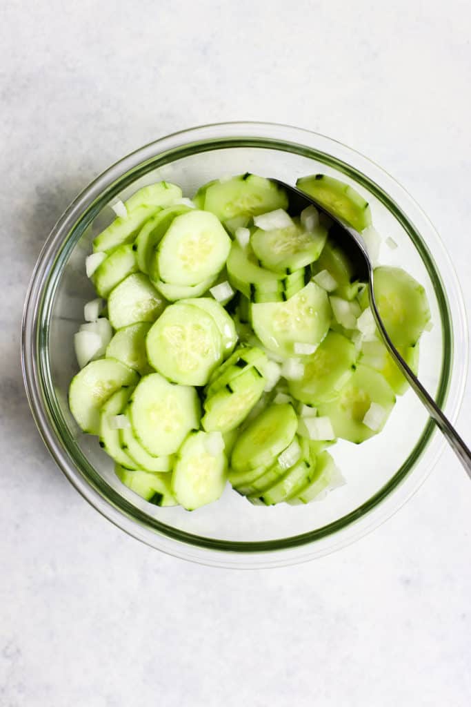 Cucumber slices and diced onion in a bowl with a spoon.