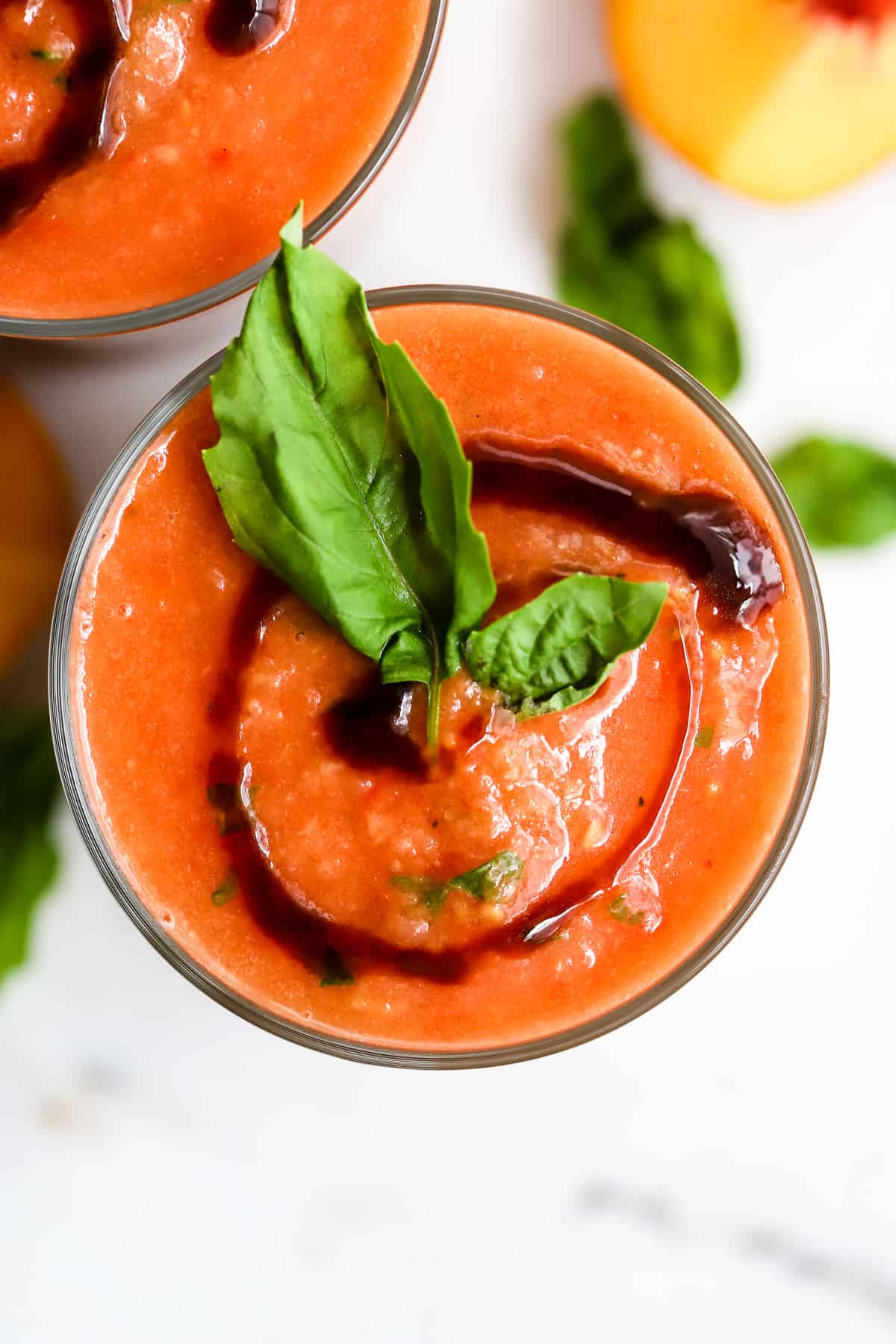 Two glasses of peach gazpacho with balsamic glaze swirl and fresh basil.