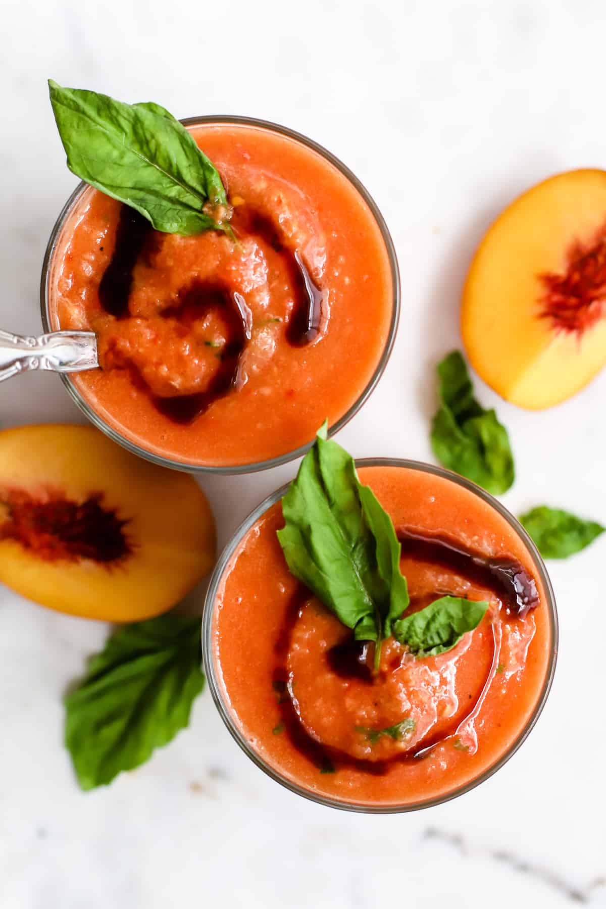 Glasses of tomato peach gazpacho drizzled with balsamic and garnished with fresh basil.
