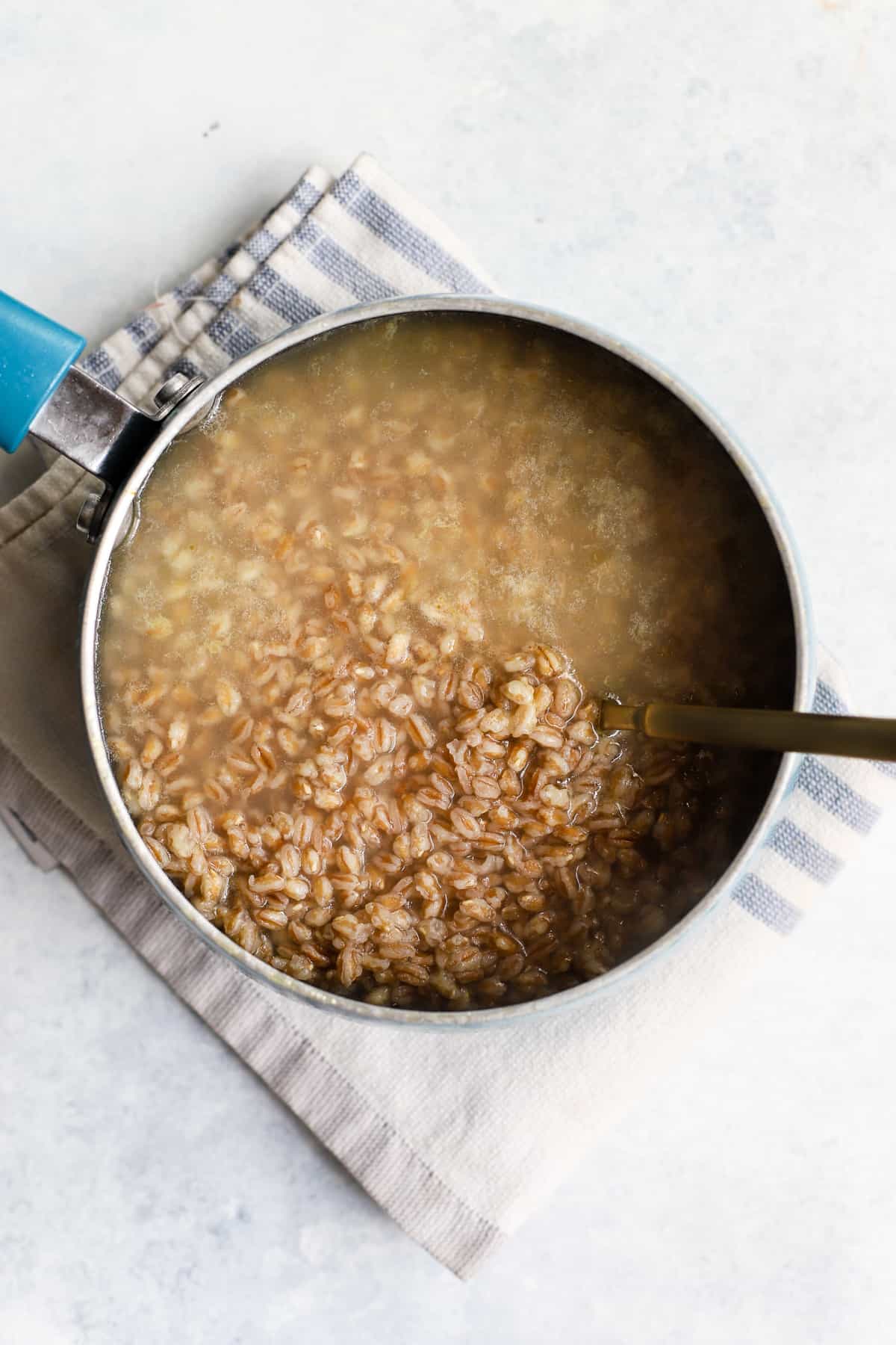 Farro cooking in small pot with a spoon.