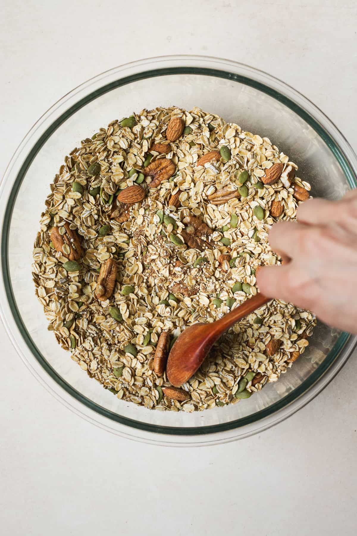 Stirring together oats, flax, quinoa, pumpkin seeds, pecans, almonds, and spices in a bowl.