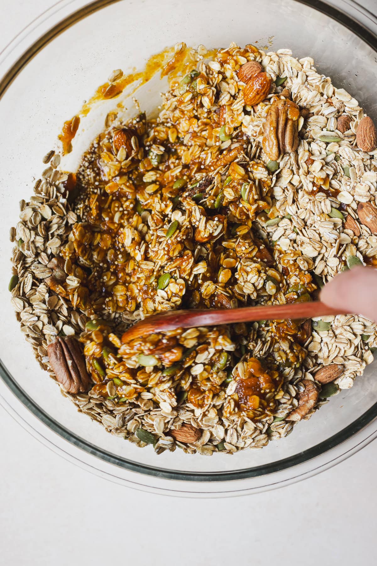 Stirring wet granola ingredients into dry ingredients in a bowl.