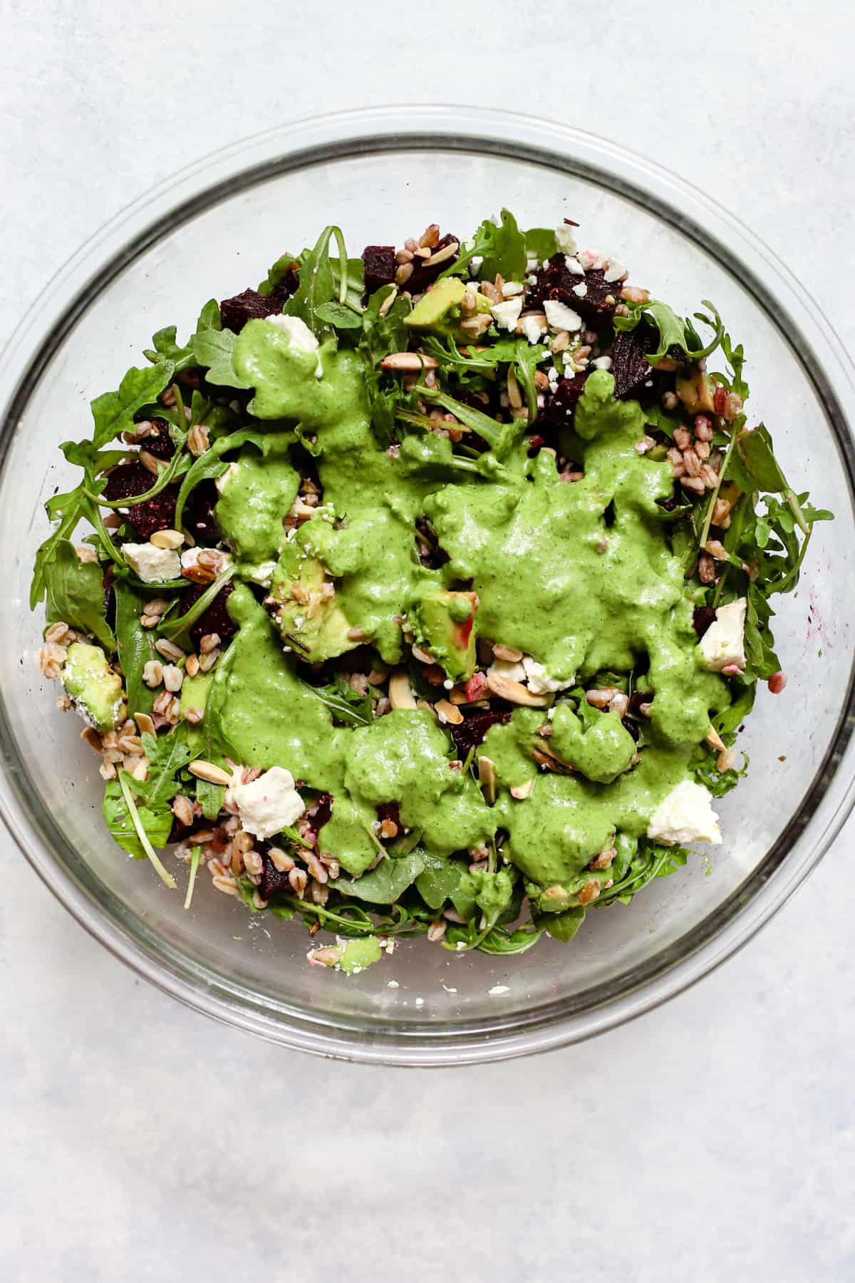 Basil lime vinaigrette poured over roasted beet and avocado salad, in a large bowl.