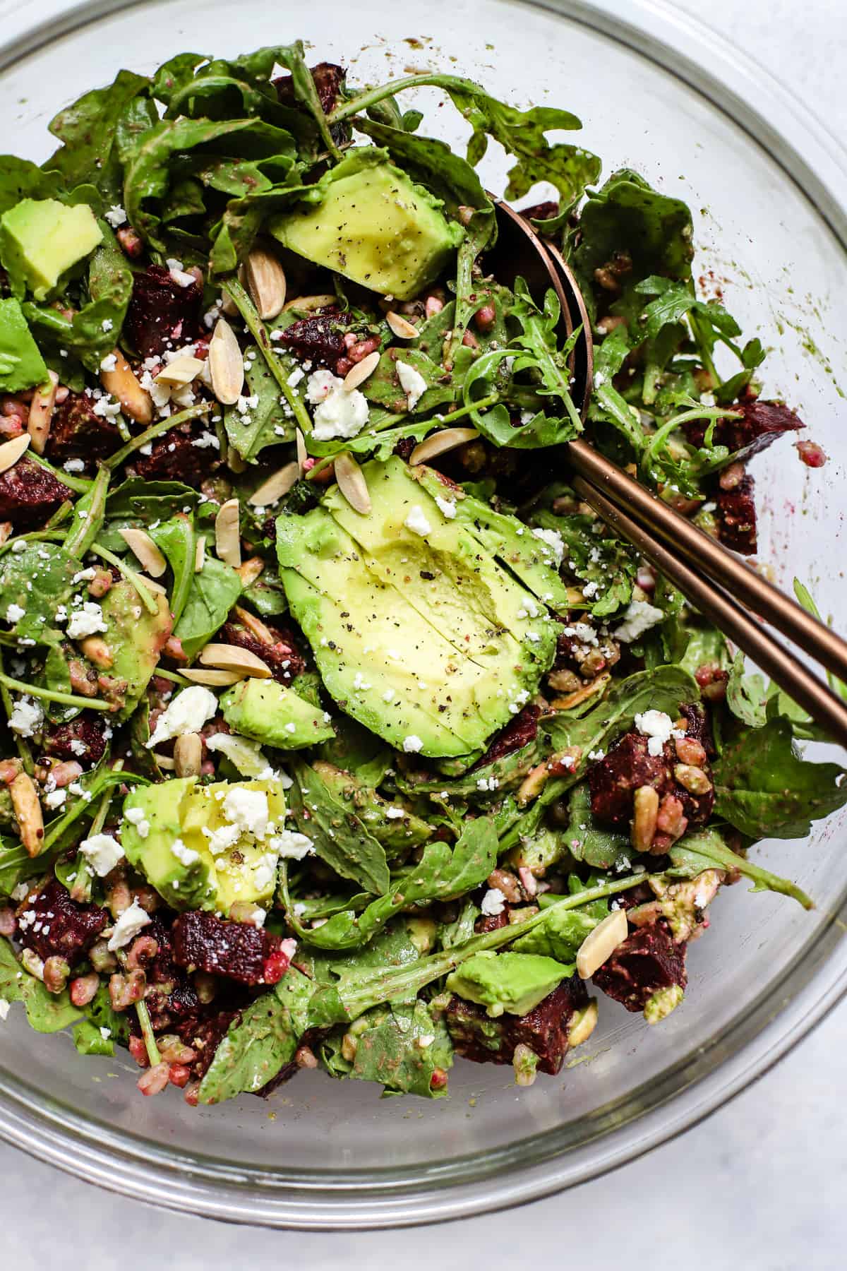 Roasted beet and avocado salad with copper serving spoons in large clear glass bowl