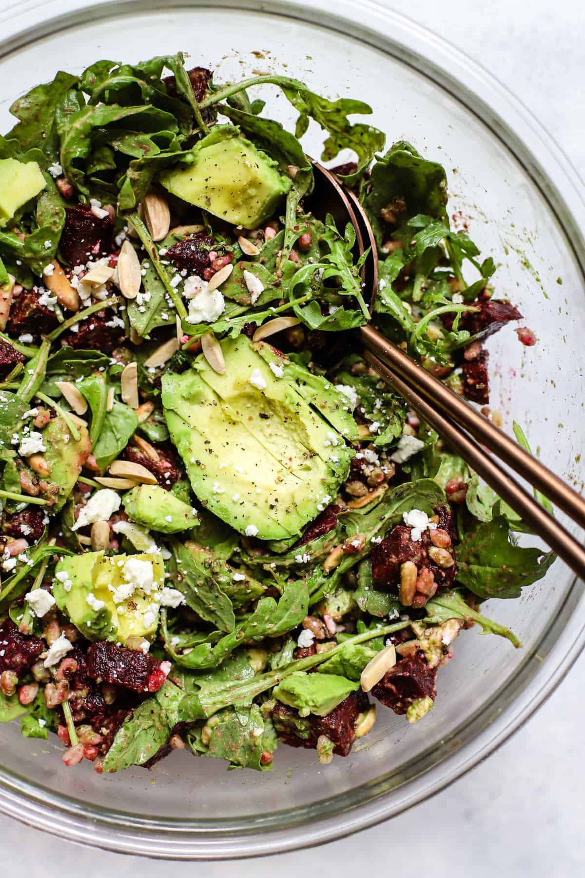 Roasted beet, avocado, and farro salad in a large bowl with serving spoons.