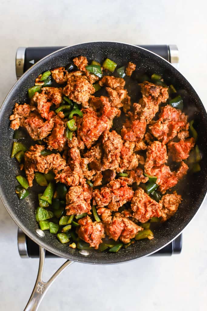 Ground chorizo cooking with poblano peppers and garlic in black sauté pan
