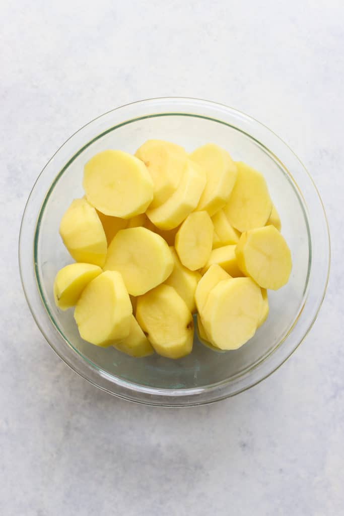 Sliced and peeled Yukon gold potatoes in clear glass bowl.