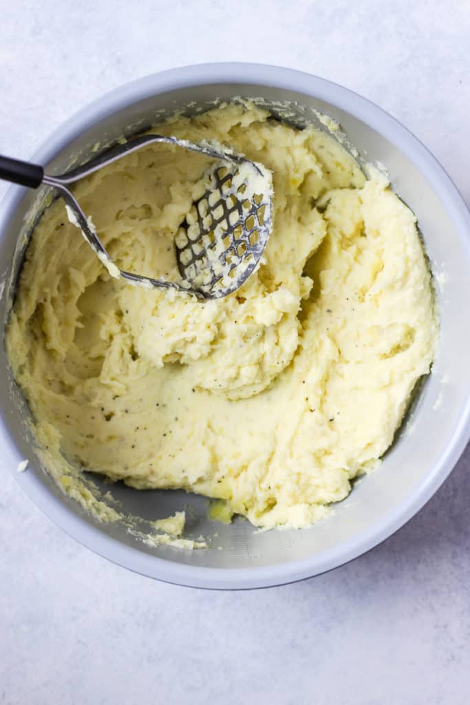 Mashed potatoes in base of pressure cooker, with potato masher.