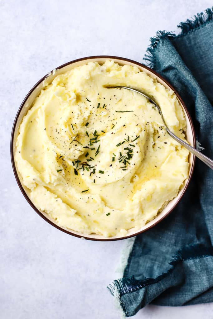 Healthy pressure cooker mashed potatoes in a bowl with butter and chives on top.