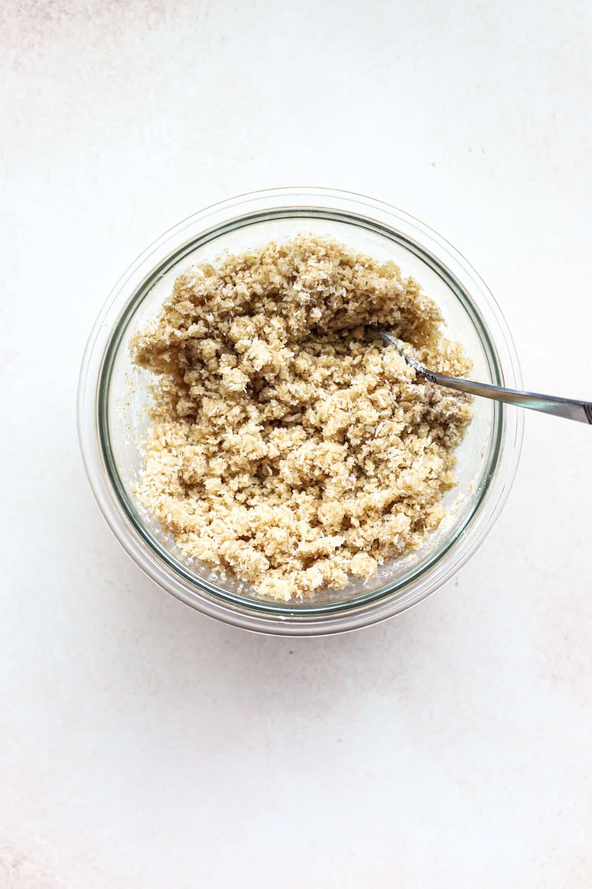 Macaroon tart crust mixed into a crumbly mixture in clear glass bowl on white-beige surface