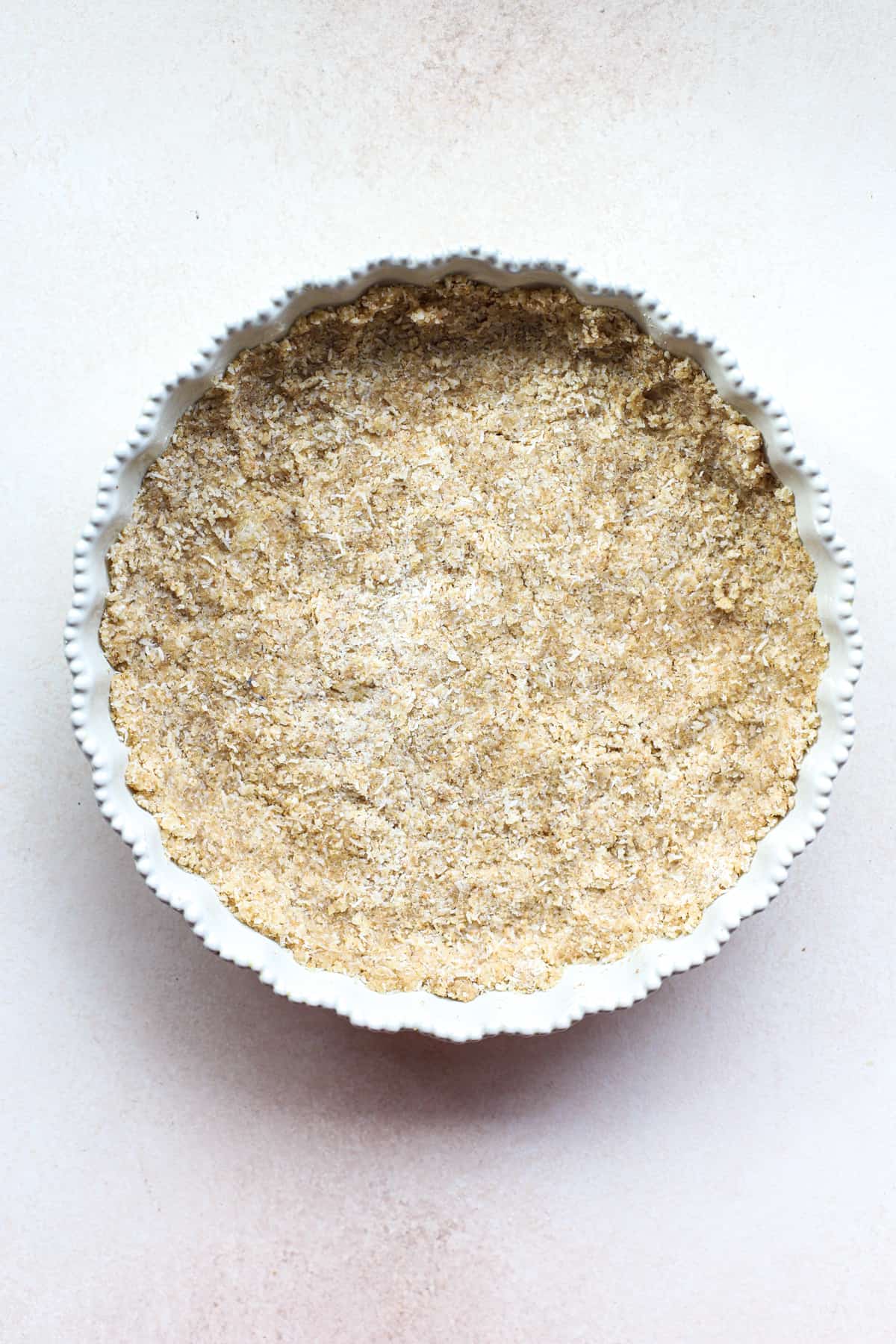 Macaroon tart crust pressed into a white ceramic tart dish, on white-beige surface