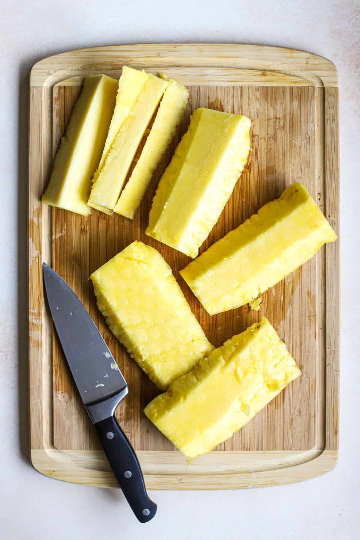 Fresh pineapple quartered lengthwise with core sliced off of each piece, on bamboo cutting board next to chef's knife