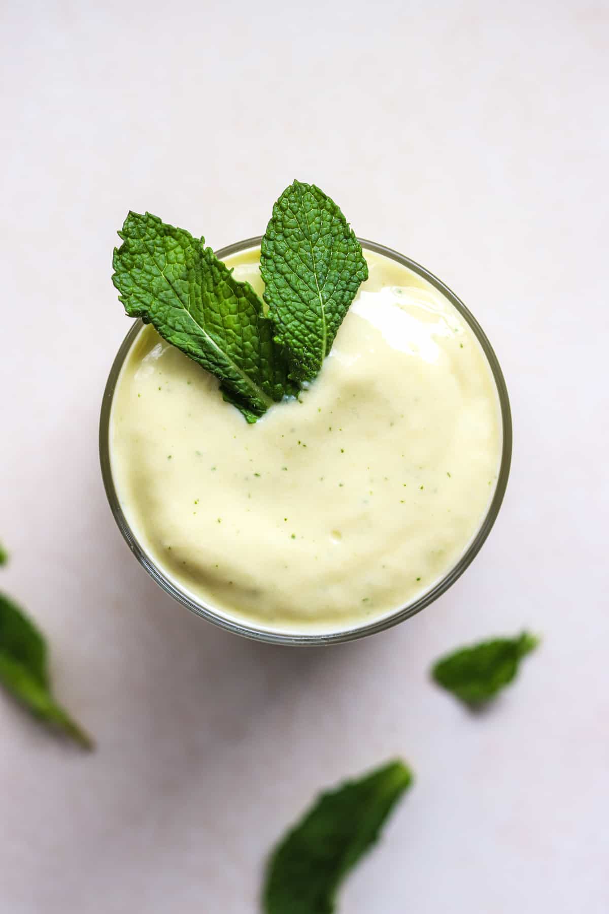 Mango mint smoothie in small glass with fresh mint leaves on top.