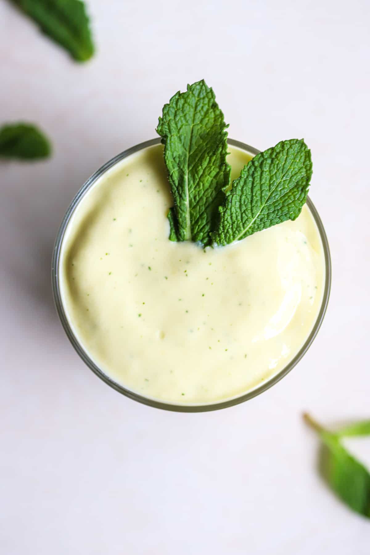 Mango mint smoothie in small glass with fresh mint leaves on top.