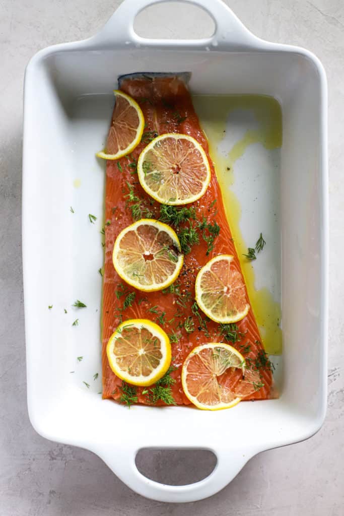 Fresh salmon with lemon and dill seasoning in a white baking dish.