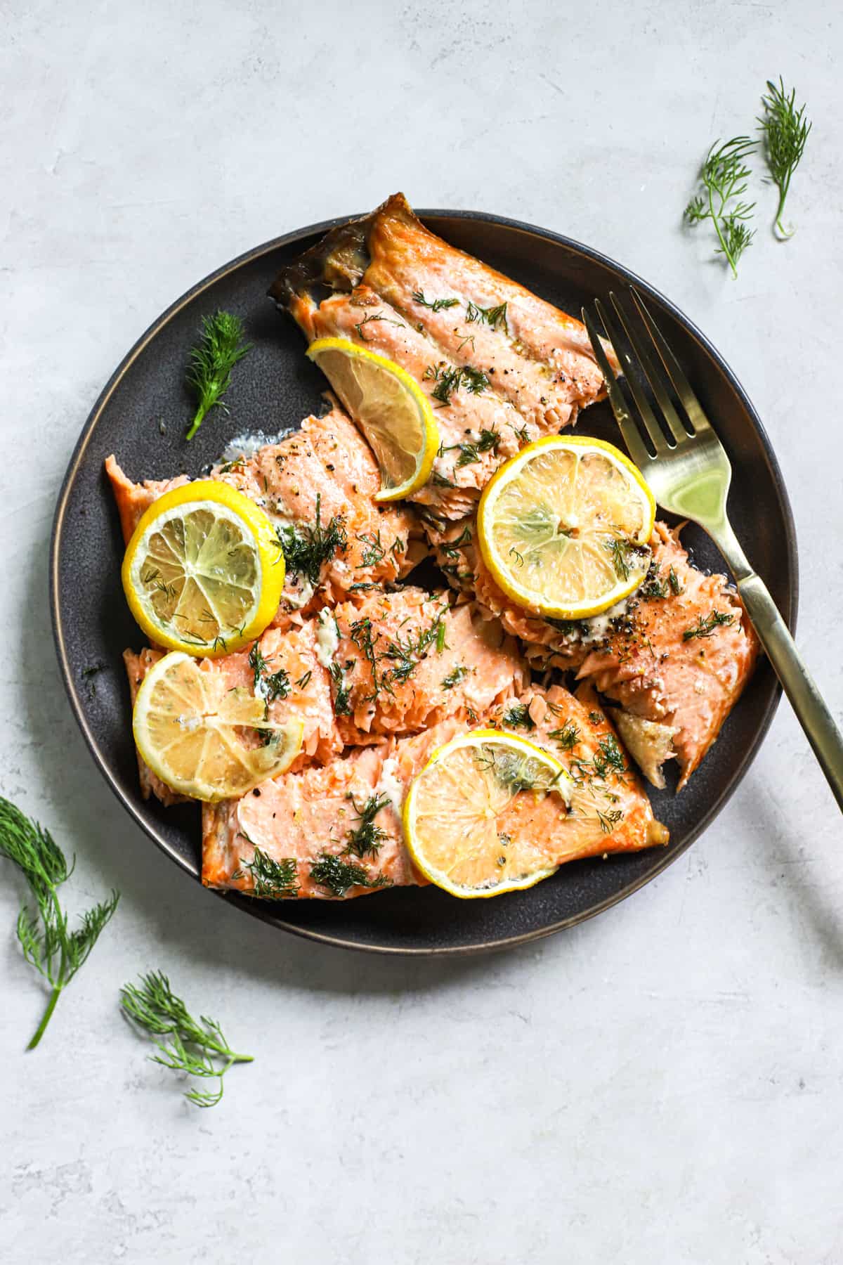Lemon dill salmon pieces topped with lemon slices, on dark gray plate with fork