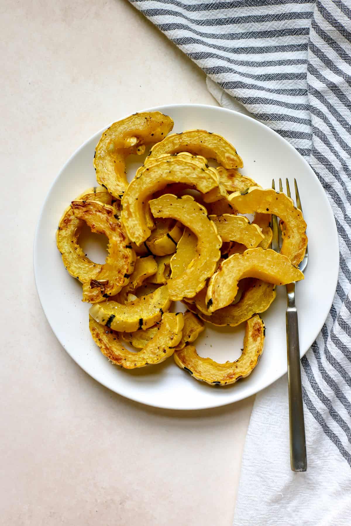 Roasted delicata squash slices on white plate with fork.