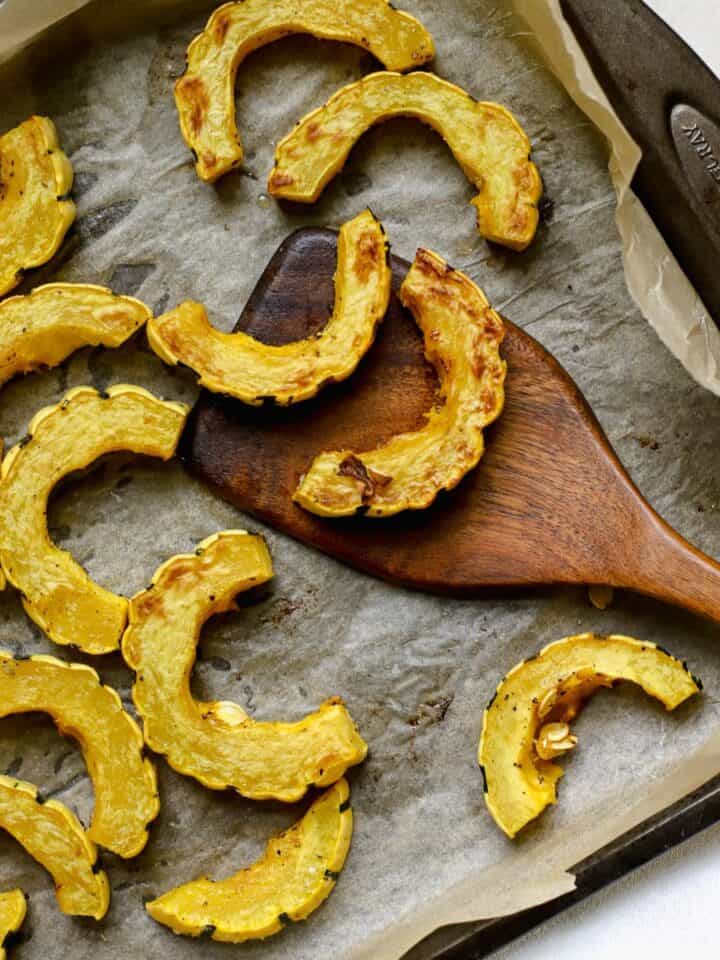 Roasted delicata squash slices on sheet pan with wooden turner.