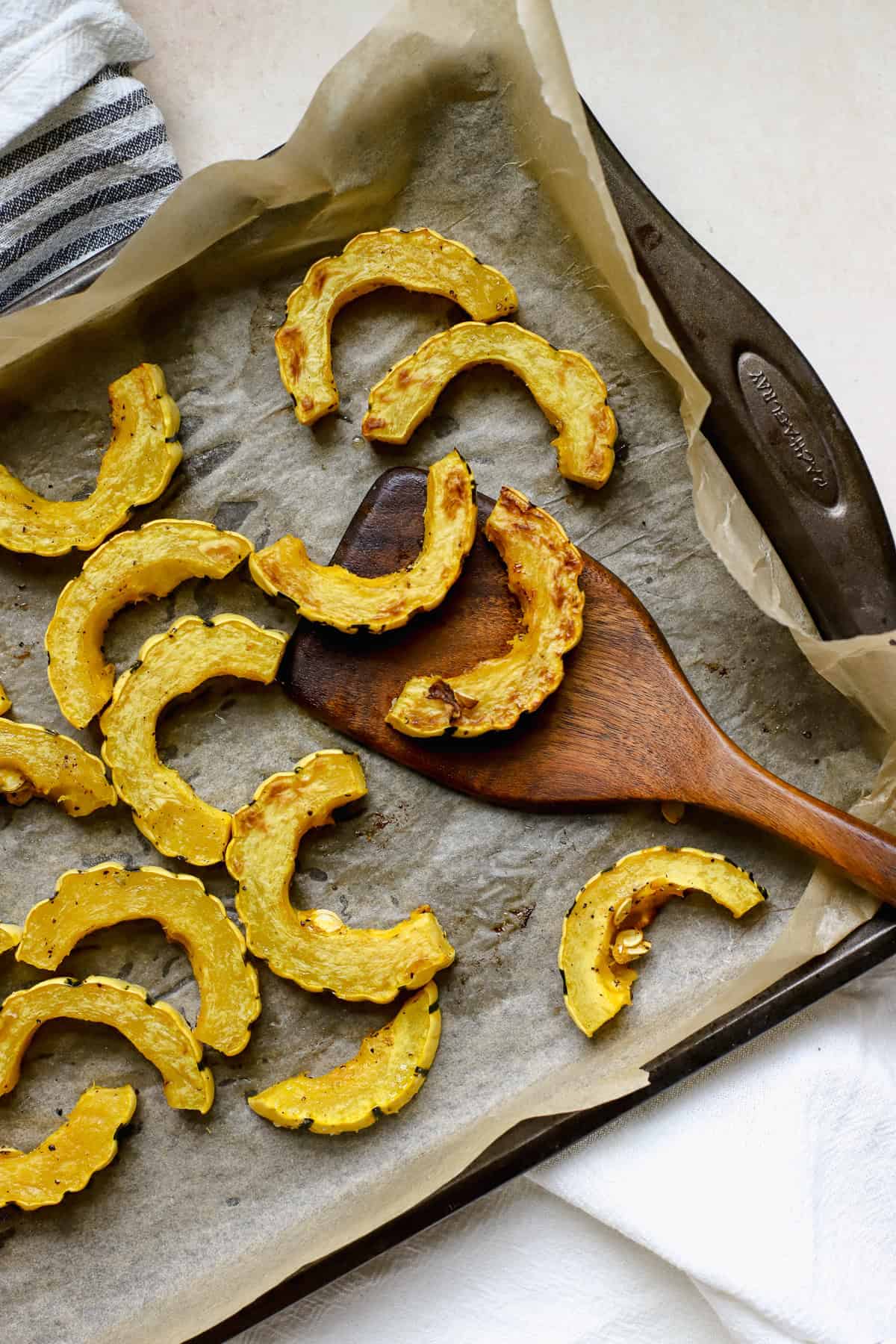 Roasted delicata squash slices on sheet pan with wooden turner.