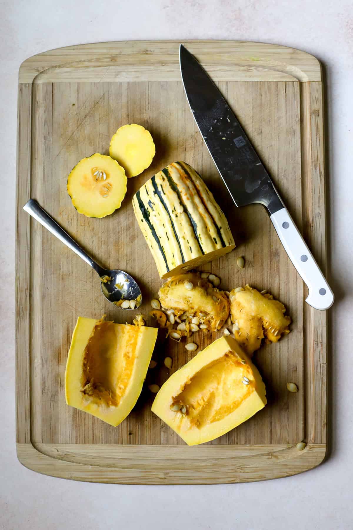 Delicata squash cut in half lengthwise with seeds being scooped out onto cutting board.