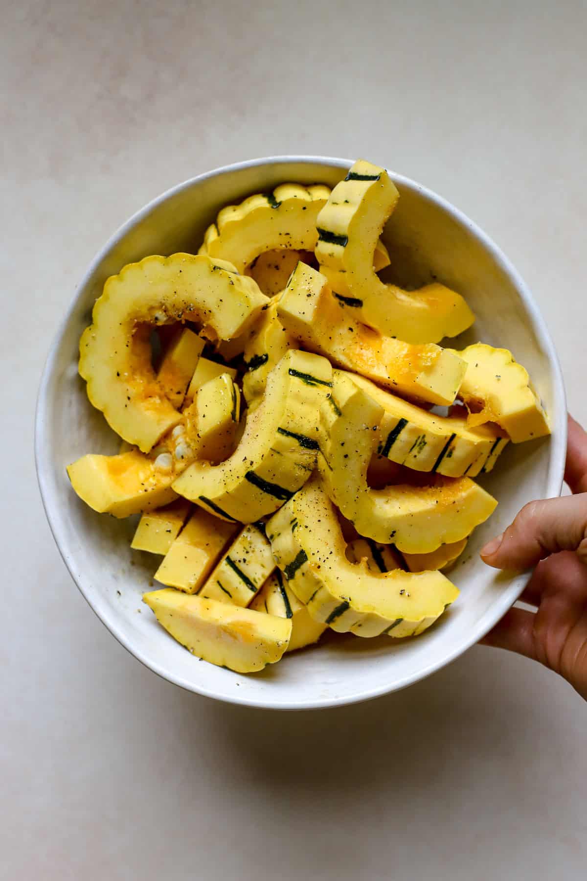 Seasoned delicata squash slices in white bowl.