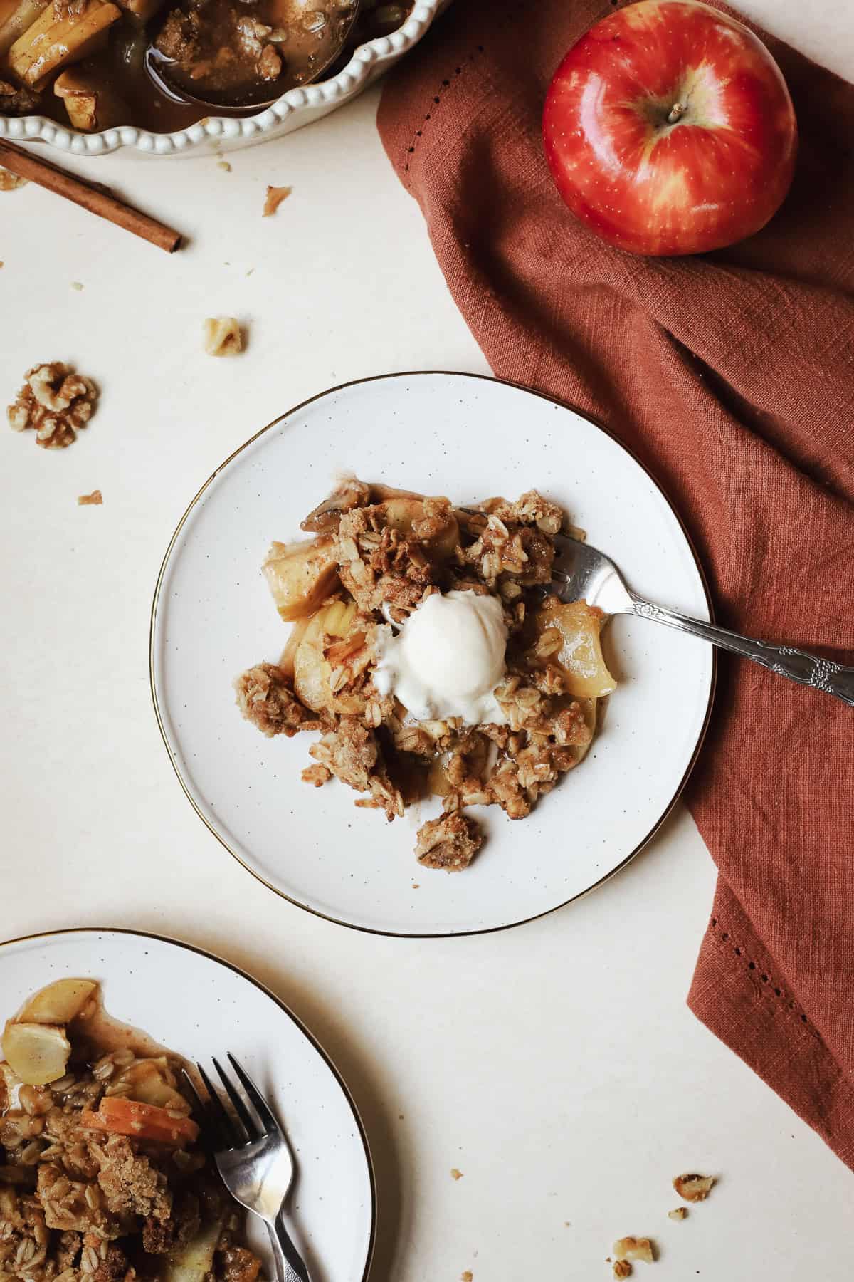 A scoop of healthy apple crisp with vanilla ice cream on dessert plate with fork.