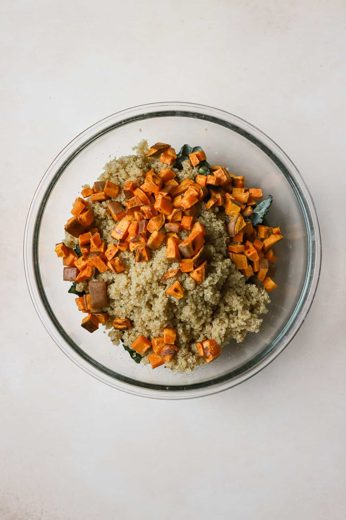 Roasted sweet potatoes and quinoa atop kale in large glass bowl.
