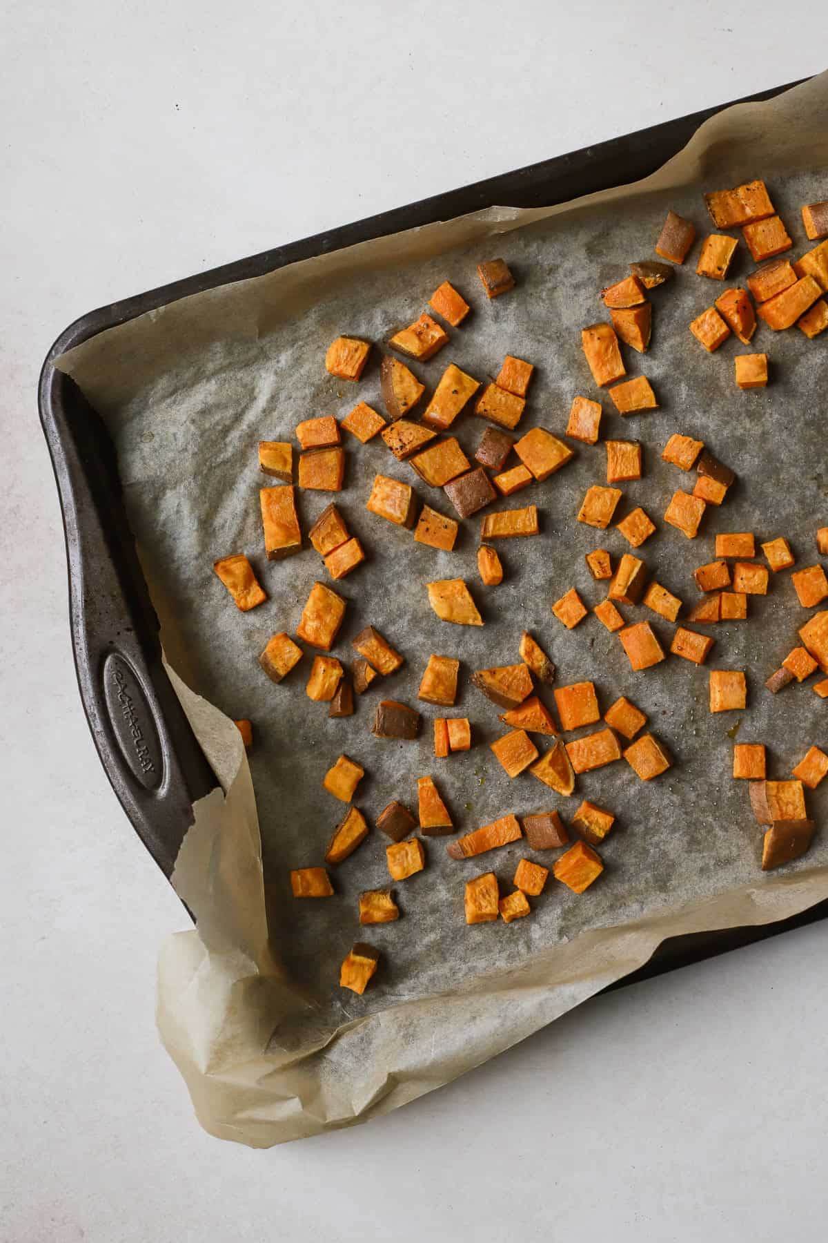 Small roasted sweet potato cubes on sheet pan.