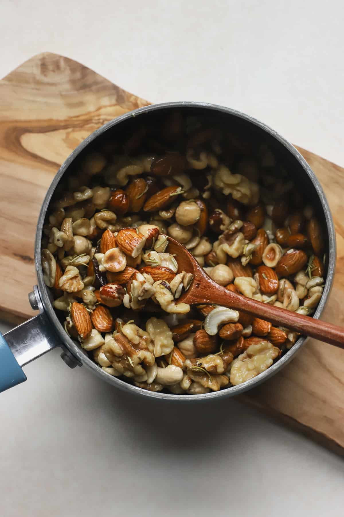 Mixed nuts in small saucepan being stirred with rosemary butter seasoning.
