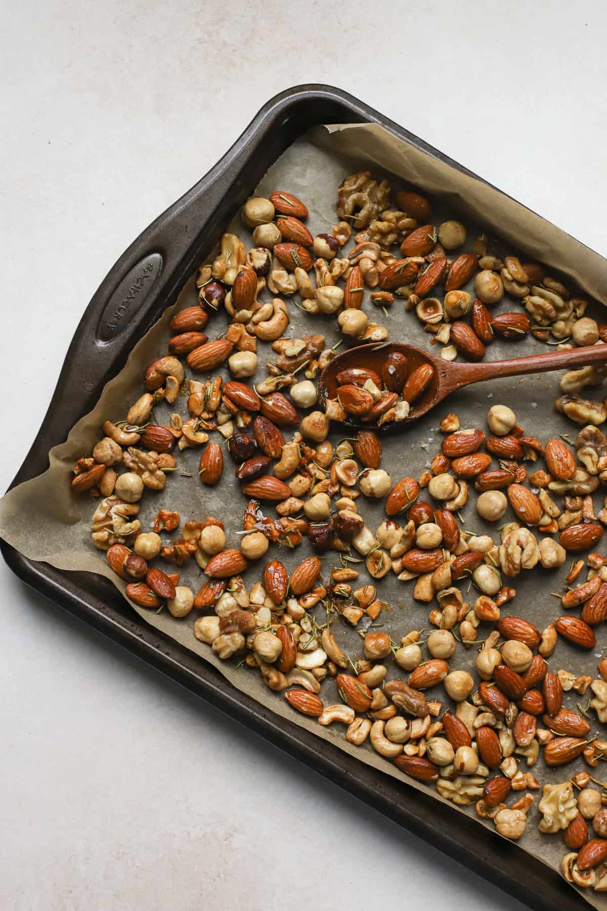 Roasted rosemary nuts on sheet pan with wooden spoon.