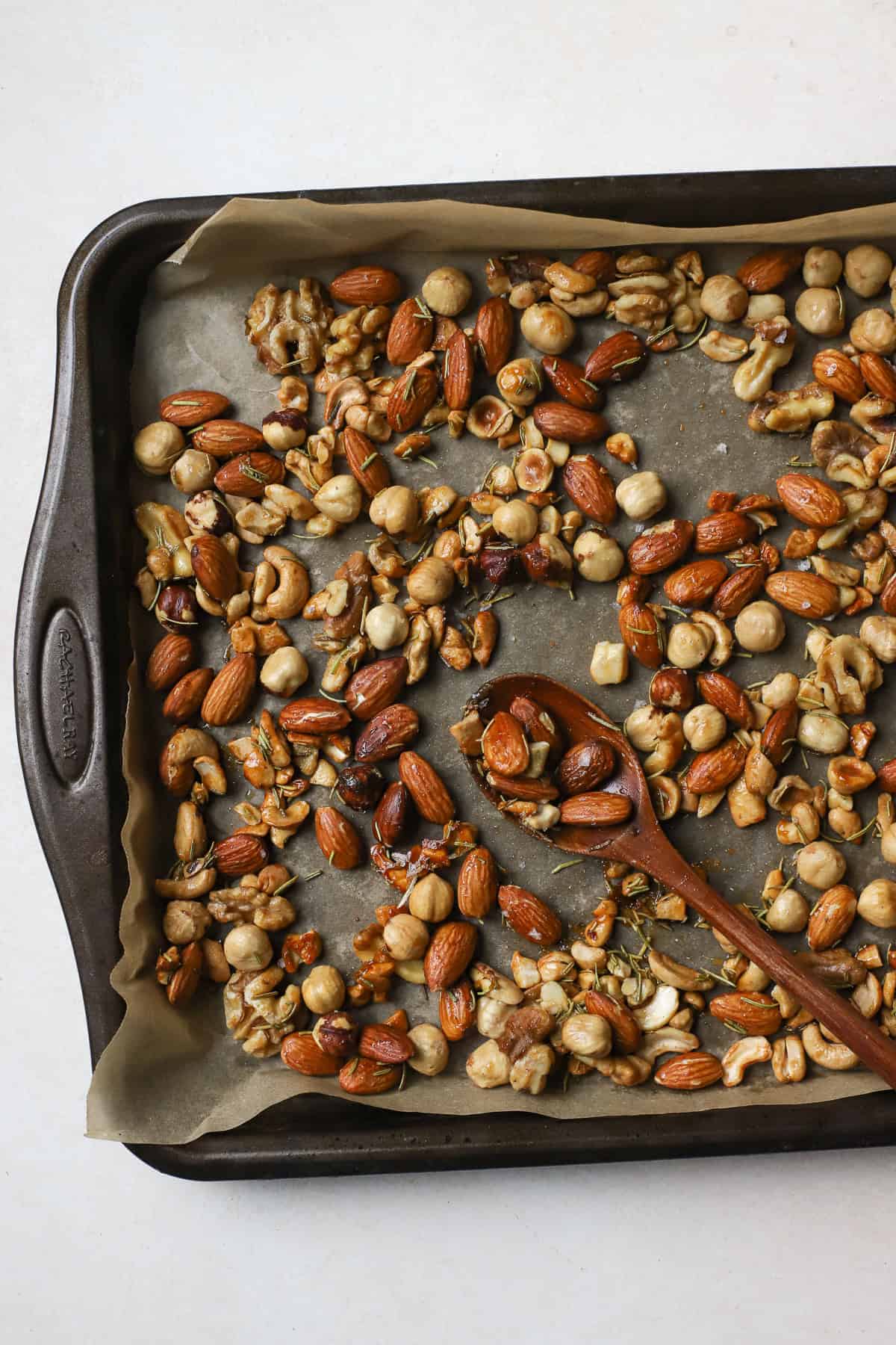 Roasted rosemary nuts on sheet pan with wooden spoon.