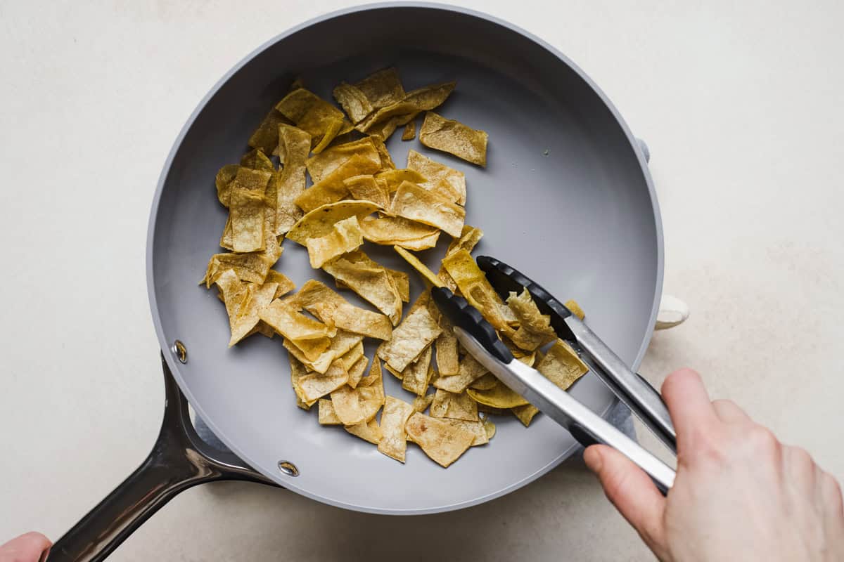 Using a tongs to pan fry thinly sliced tortilla strips for chicken tortilla soup.