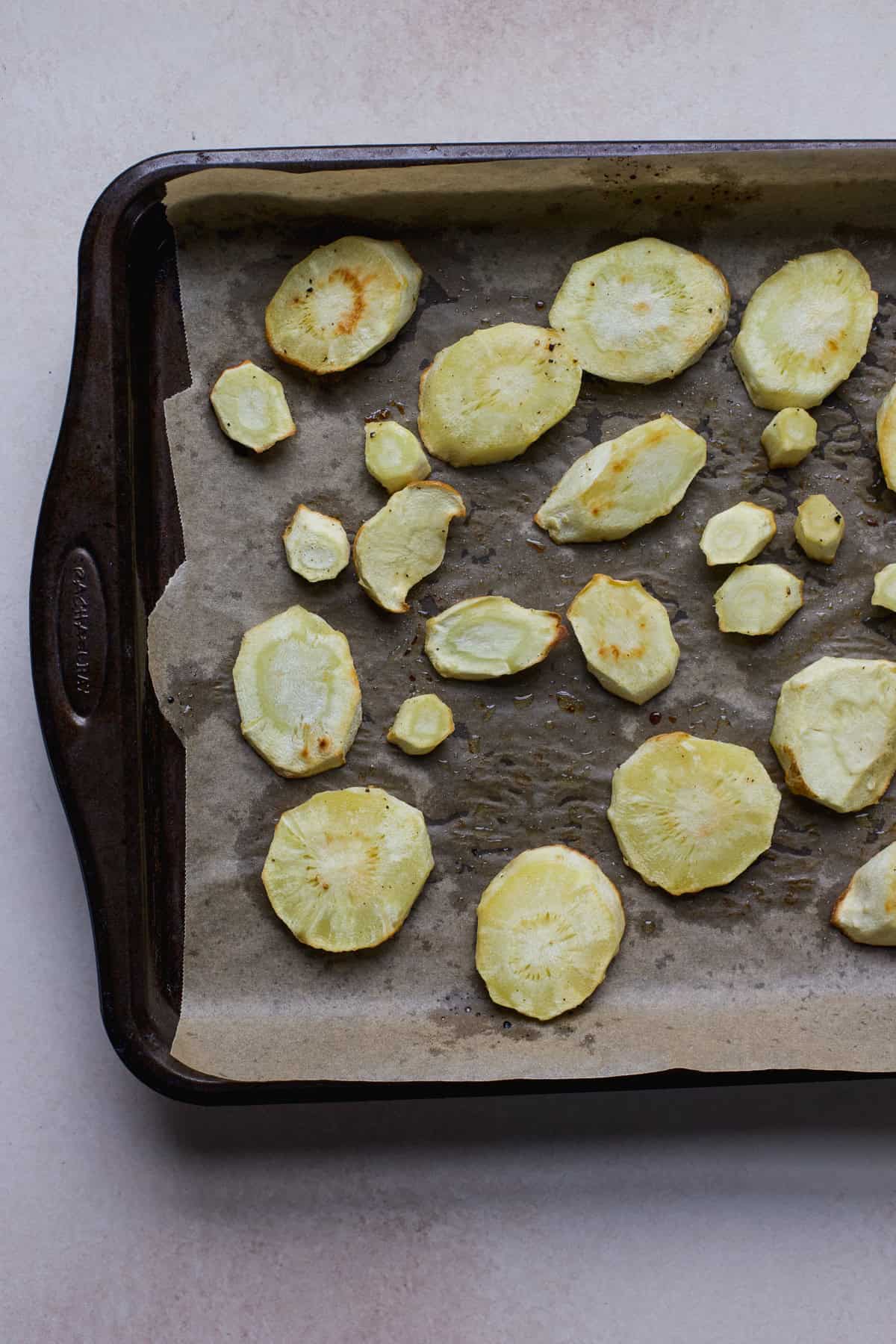 Roasted parsnip slices on sheet pan.