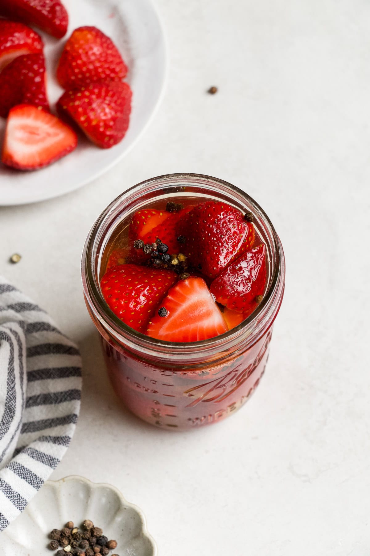 Pickled strawberries in a jar with black peppercorns.