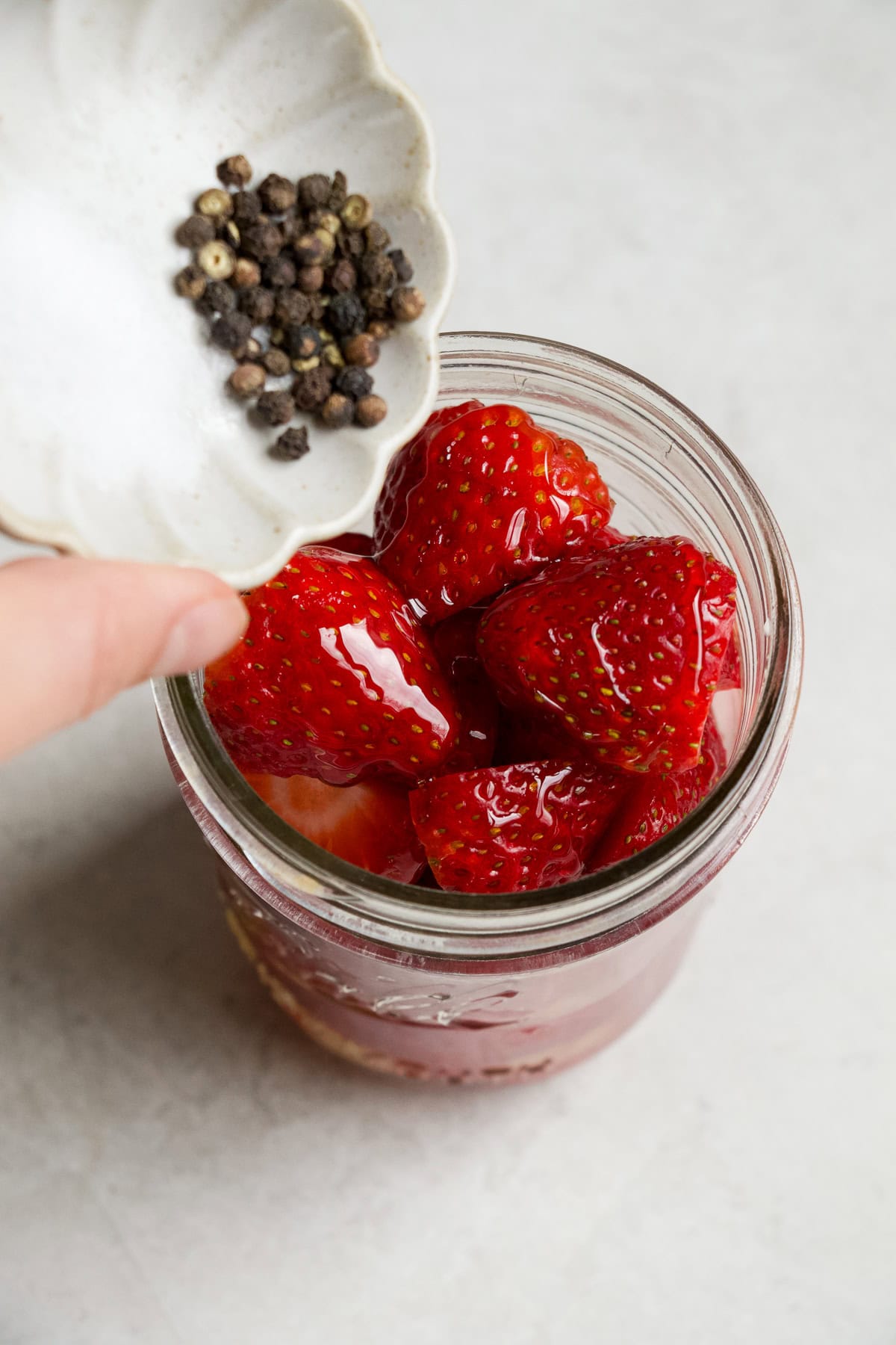 Adding black peppercorns to pickled strawberry jar.