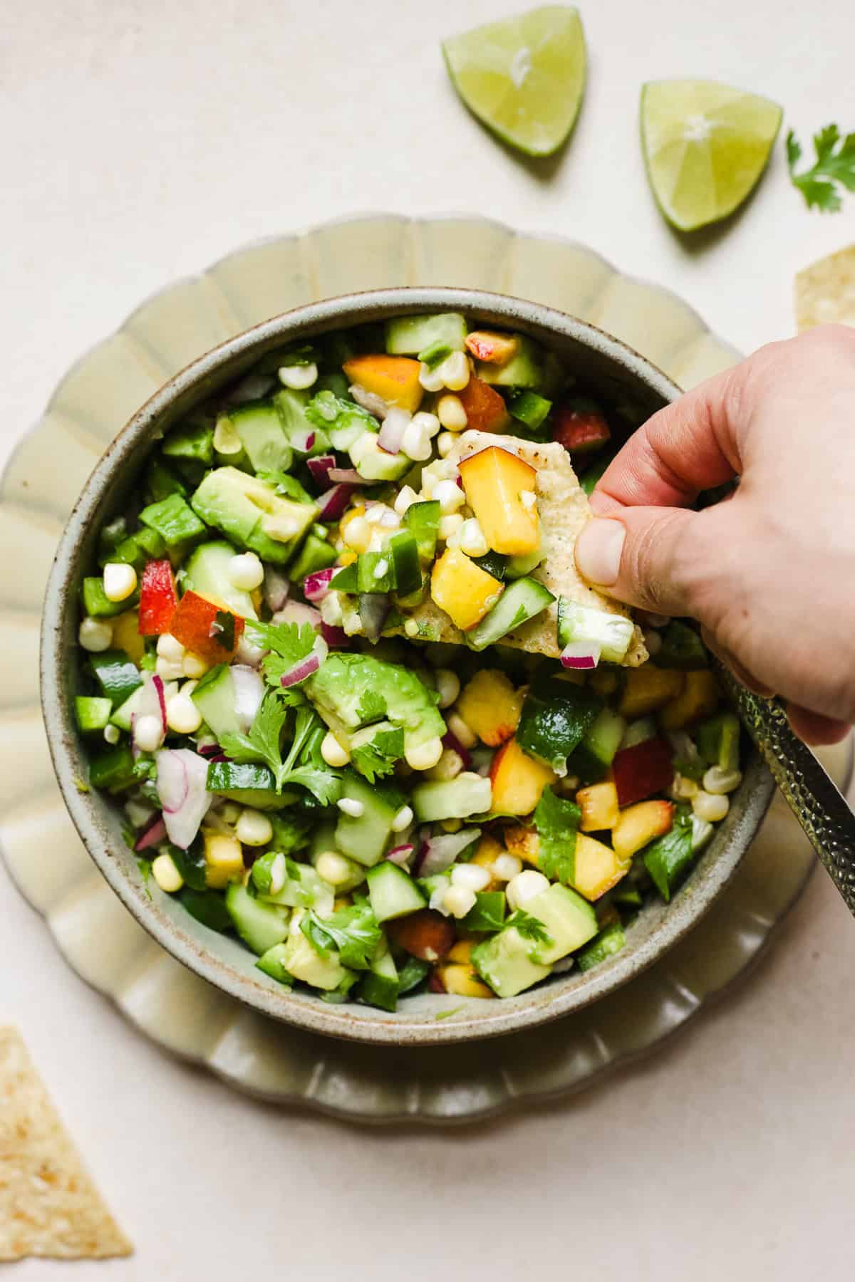 Hand dipping a tortilla chip into fresh peach salsa with corn and avocado.