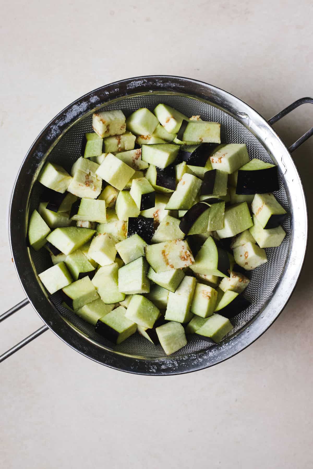 Salted eggplant cubes in a strainer.