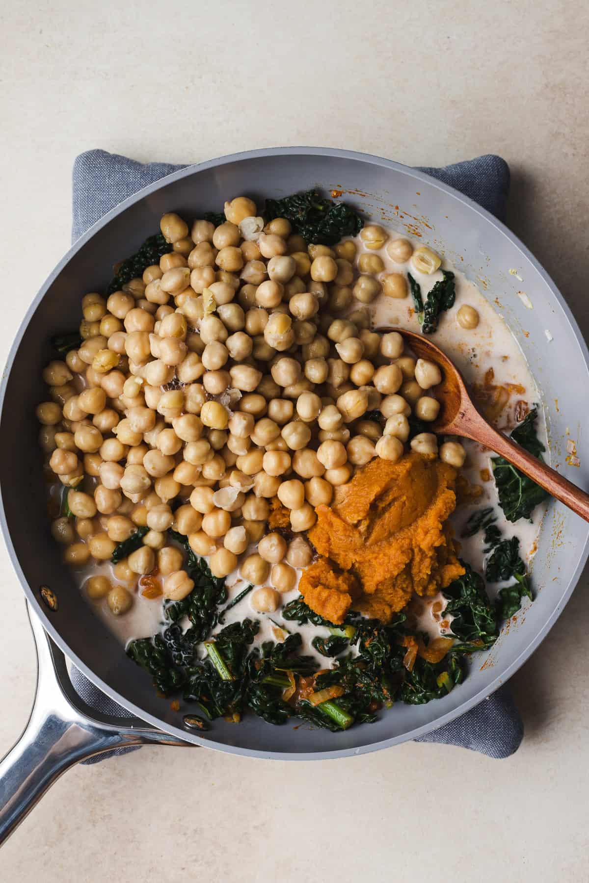 Adding chickpeas, canned pumpkin, coconut milk, and soy sauce to the skillet.