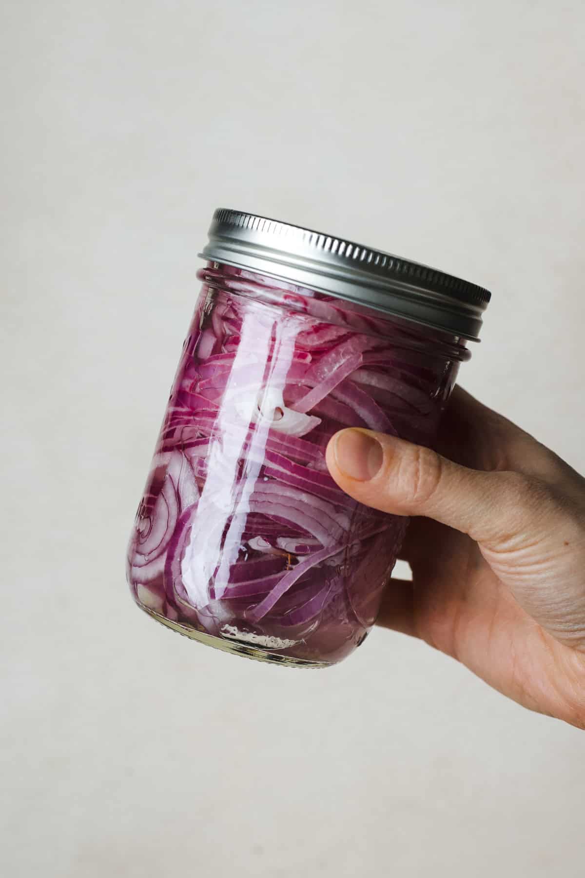 Hand shaking a jar to mix pickled red onion ingredients.